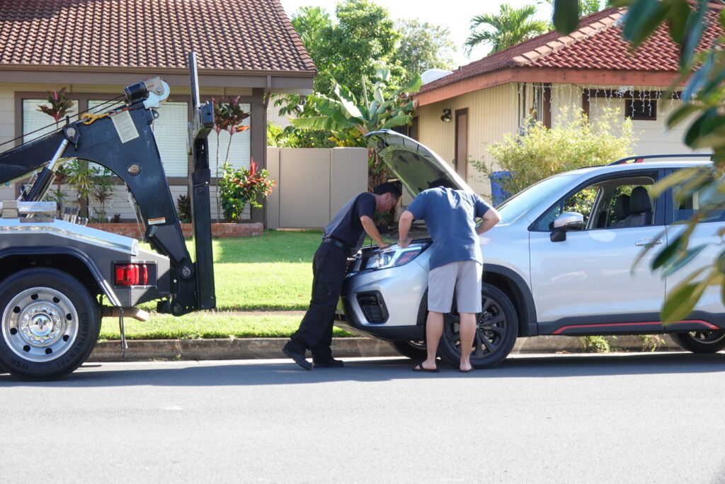 man looking under the hood of his car with mechanic and tow truck